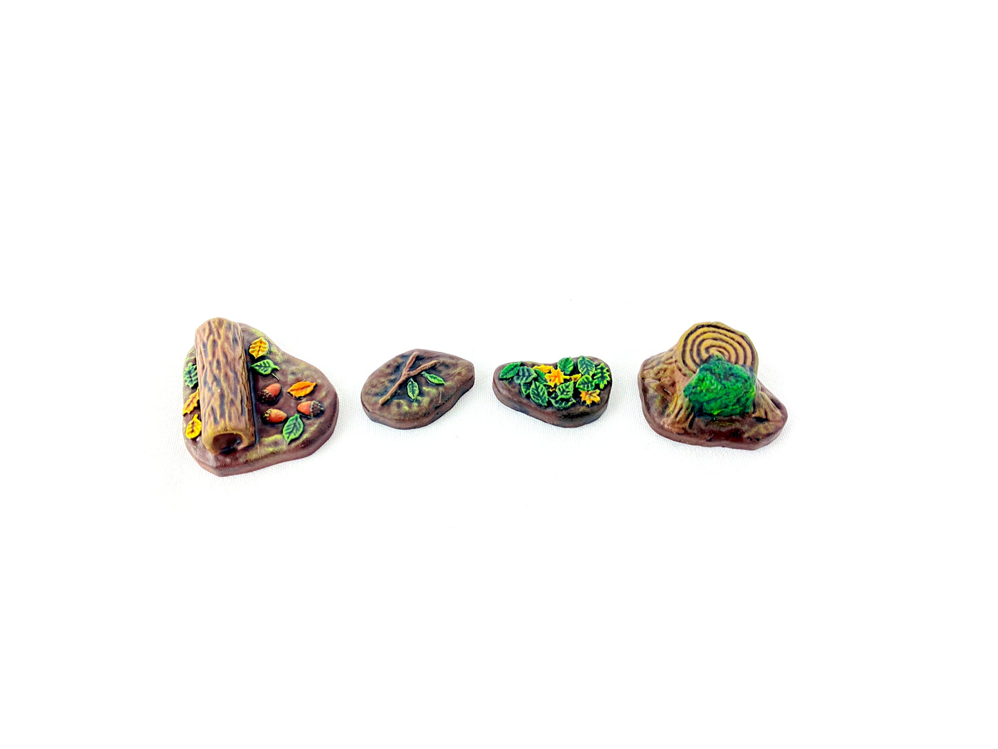 Vier bemalte Waldboden-Bases aus dem Scatter-Set: liegender Baumstamm mit Blättern, Ast mit Blättern, kleiner Laufring im Boden und Baumstamm mit Moos an der Seite, detailreich für Tabletop- und Rollenspiel-Szenarien.